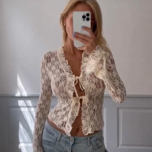 Vit spetsblus med knytning - Säljer en elegant vit spetsblus med knytning framtill. Blusen har långa ärmar och ett vackert spetsmönster som ger en romantisk känsla. Perfekt för att lyfta vilken outfit som helst.