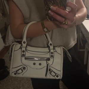 Vit handväska  - Snygg vit handväska med svarta detaljer och dragkedja framtill. Väskan har även ett längre band till!❣️