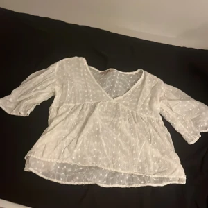 Vit blus från KappAhl str S - Säljer en söt vit blus från KappAhl str S med v-ringning och trekvartsärmar. Blusen har ett diskret blommönster och är tillverkad i ett lätt och luftigt material. Perfekt för vår och sommar!