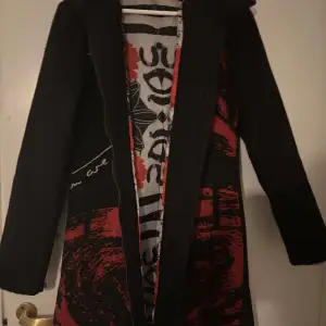 Snygg svart kappa från Desigual med unikt rött och svart mönster på insidan. Jackan har långa ärmar och en stilren design som passar perfekt för höst och vinter. Den har en dragkedja framtill och är tillverkad i ett mjukt material för extra komfort.