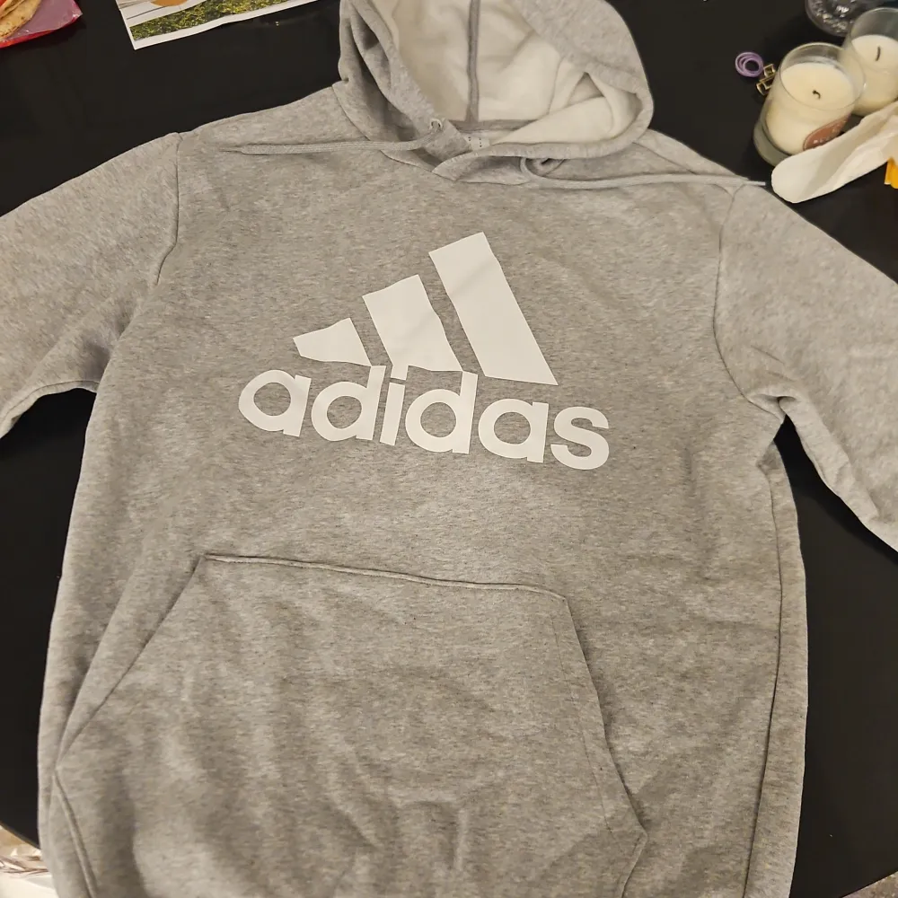 Säljer en grå hoodie från Adidas med den klassiska loggan i vitt på framsidan. Tröjan har en stor ficka framtill och en justerbar huva. Perfekt för en avslappnad stil.. Neuletakit & Villapaidat.