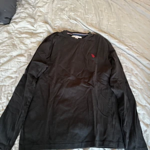 Svart långärmad tröja från Ralph Lauren - Säljer en stilren svart långärmad tröja från Ralph Lauren med en liten röd broderad logga på bröstet. Perfekt för en avslappnad och snygg look. Passar bra till jeans eller chinos.