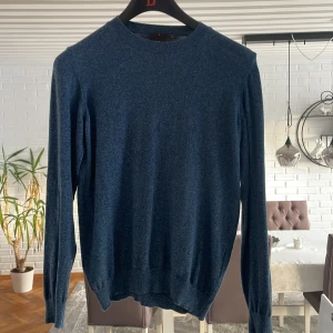 Blå tröja från Oscar Jacobson - Säljer en stilren blå tröja från Oscar Jacobson. Tröjan är tillverkad i Italien och har en klassisk design med långa ärmar och rund hals. Perfekt för en elegant och avslappnad look.