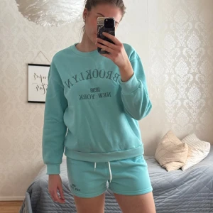 Turkos sweatshirt med Brooklyn-tryck - Säljer en snygg turkos sweatshirt med texten 'Brooklyn 1988 New York' tryckt på framsidan. Tröjan har långa ärmar och en rund halsringning. Perfekt för en avslappnad stil.