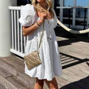 Vit kortklänning med puffärmar - Säljer en söt vit kortklänning med puffiga kortärmar och en luftig passform. Klänningen har en fyrkantig urringning och knytning framtill, perfekt för sommarens varma dagar. Den är gjord i ett lätt och bekvämt material som ger en avslappnad look. Perfekt studentklänning!!!!