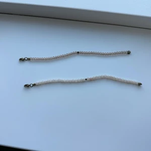 Två rosa armband med pärlor - Säljer två eleganta armband med små rosa pärlor. Armbanden har en enkel och stilren design med metallspänne i ändarna. Perfekta för att ge en subtil touch av färg till din outfit.
