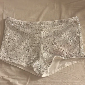 Vita paljettshorts - Snygga vita shorts täckta med glittrande paljetter. De har en tight passform och är tillverkade i ett syntetmaterial som ger en bekväm känsla. perfekt för en konsert outfit 