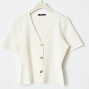 Gina topp - Snygg vit kofta från Gina Tricot med korta ärmar och v-ringning. Den har dekorativa knappar framtill och en figurnära passform. Perfekt för en stilren look. Endast testad!💗