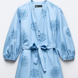 Blå klänning med broderade detaljer från Zara - Snygg ljusblå klänning från Zara med broderade blommönster och ett knytbälte i midjan. Klänningen har trekvartsärmar och en avslappnad passform. Perfekt för vår och sommar! Helt oanvänd.
