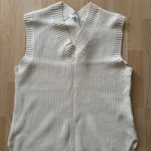 Vit stickad väst H&M - Säljer en stilren vit stickad väst med v-ringning. Perfekt för lager-på-lager och ger en snygg touch till din outfit. Passar bra till både vardag och mer uppklädda tillfällen.