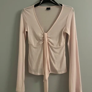 Rosa långärmad topp med knyt - Snygg rosa långärmad topp med v-ringning och knyt framtill. Perfekt för en stilren look. Tillverkad i ett mjukt och bekvämt material.