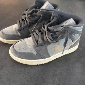 Grå Nike Air Jordan 1 Mid - Snygga grå Nike Air Jordan 1 Mid med en ljusbrun swoosh. De är utrustade med snörning och har en bekväm sula i kontrasterande färg. Box ingår.