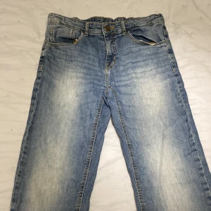 Blå jeansbyxor från Zara Boys - Säljer ett par ljusblå jeansbyxor från Zara Boys i storlek 164 cm. Byxorna har en klassisk femficksdesign och justerbar midja med knapp. Perfekta för en avslappnad stil.