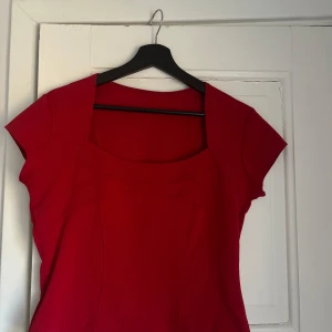 Röd klänning med korta ärmar - Snygg röd klänning med korta ärmar och en stilren design. Perfekt för att sticka ut med sin klara färg. Klänningen har en enkel och elegant skärning som ger en smickrande passform.står ej storlek eller märke men uppskattar m