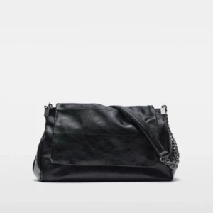 Svart axelväska med kedjedetaljer - Snygg svart axelväska i skinn med kedjedetaljer. Väskan har en praktisk dragkedja och en stilren design som passar perfekt för alla tillfällen. Den har en justerbar axelrem med kedjor som ger en cool touch.