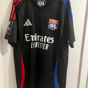 Fotbollströja Lyon Cherki - Lyons bortaställ 24/25 med Rayan Cherki på ryggen. Autentisk och oanvänd tröja köpt från unisport. 