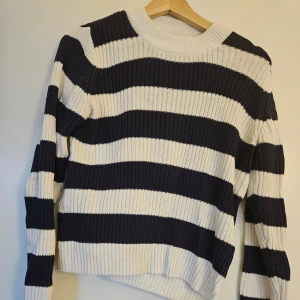 Randig stickad tröja från 157 - Säljer en snygg randig stickad tröja från 157 i svart och vitt. Tröjan har en ribbad struktur och långa ärmar, perfekt för kyligare dagar. Den har en klassisk rund halsringning och är både stilren och bekväm.