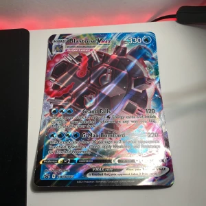 Blastoise VMAX Pokémonkort - Säljer ett Blastoise VMAX Pokémonkort med holografisk design. Kortet har 330 HP och inkluderar attacker som Grand Falls och G-Max Bombard. Perfekt för samlare eller spelare som vill förstärka sin kortlek. Kortet är en del av Sword & Shield-serien.ingen frakt