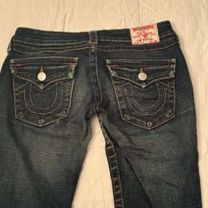Mörkblå jeans från True Religion - Snygga mörkblå jeans från True Religion med ikoniska bakfickor och kontrastsömmar. De har en låg midja och lite botcut men inte riktigt super fina insydda lite i midjan men tar bort vid önskan skriv vid minsta lilla funderinga