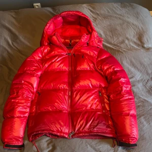 Röd dunjacka från Polo Ralph Lauren - Säljer en snygg röd dunjacka från Polo Ralph Lauren. Jackan har en glansig finish,Perfekt för kyliga dagar. Jackan är i fint skick men har nått litet märke men släpper inte dun. Nypris är 6000