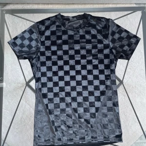 Svart t-shirt med rutmönster - Snygg svart t-shirt med ett coolt rutmönster. Perfekt för en stilren look. Kortärmad och tillverkad i ett mjukt material som ger en skön känsla. Passar bra till både jeans och shorts.