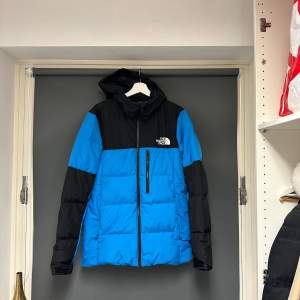 Säljer en snygg blå och svart pufferjacka från The North Face. Jackan har en dragkedja framtill och är perfekt för kalla dagar. Den är i nyskick och har en normal passform. Perfekt för vintern och hösten! Bara använt den i 2 dagar när jag va på skidsemester. 