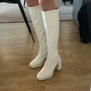Vita stövlar med klack - Säljer ett par vita stövlar  med hög klack och dragkedja på sidan. De är knähöga och har en stilren design, perfekt för både vardag och fest. Några märken finns på tån, men de är fortfarande i bra skick. Nypris 540kr