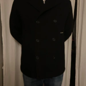 Svart skepparkavaj Armani Exchange  - Säljer en stilren svart skepparkavaj i ull. Den har en klassisk dubbelknäppning med stora knappar och en snygg krage. Perfekt för höst och vinter, och funkar både till vardags och fest. Passar bra över en tröja eller skjorta. 🖤