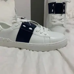 Säljer ett par snygga Valentino Garavani sneakers i vitt med blå detaljer. Skorna är i nyskick och har en stilren design med snörning. Perfekta för både vardag och fest! Kommer med originalförpackning. Helt nya.