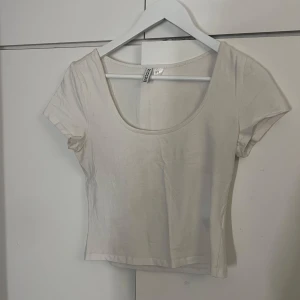 Vit kortärmad topp från H&M - Säljer en enkel och stilren vit topp från H&M Divided. Den är kortärmad och har en rund halsringning.. Toppen är i bra skick och gjord av mjukt bomullsmaterial.