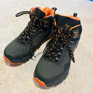 Svarta och orangea kängor från Engelsons - Säljer ett par robusta kängor från Engelsons i storlek 37. De är svarta med orangea detaljer och har en slitstark sula perfekt för utomhusaktiviteter. Skorna har snörning och en bekväm passform, idealiska för höst- och vinterväder. Nya utan kvitto. Endast provade. 599kr i nypris 