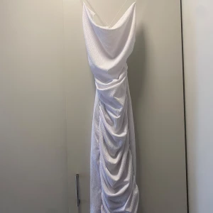 Vit långklänning med drapering - Säljer en elegant vit långklänning med vacker drapering framtill. Klänningen har en stilren design med smala axelband och en mjuk, flytande passform. Perfekt för sommarens fester eller en speciell kväll. Den är i nyskick och redo att bäras av någon som vill känna sig extra glamorös. Använd 1 gång