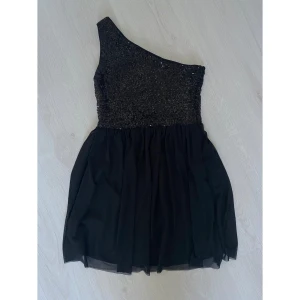 Svart klänning  - Svart enärmad klänning med paljetter och tyllkjol från Model Behaviour i strl XS. Dragkedja i ena sidan, ganska kort i modellen. Använd en gång på nyårsafton så i väldigt fint skick.   Kommer från djur- och rökfritt hem, tvättad parfymfritt.
