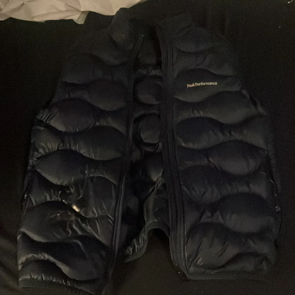Säljer en svart dunväst från Peak Performance. Västen har en dragkedja framtill och är quiltad för extra värme. Perfekt för höst och vinter. Den är i välanvänt skick med några märken på framsidan. Passar bra för både vardag och utomhusaktiviteter.. Takit.