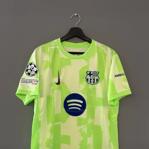 Fotbollströja Barcelona Lamine yamal - Säljer en grön FC Barcelona fotbollströja med korta ärmar. Tröjan har klubbens emblem och sponsorlogga på framsidan samt spelarnamnet och nummer 19 på baksidan. UEFA-märke på ärmen. Replika Storlek M och helt ny med tagg