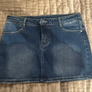 Blå jeanskjol - Snygg blå jeanskjol med klassisk design. Kjolen har en kort längd och är utrustad med både fram- och bakfickor. Perfekt för en avslappnad stil. Den är i storlek L men jag har S o den sitter perfekt på mig så den är väldigt liten i storlek
