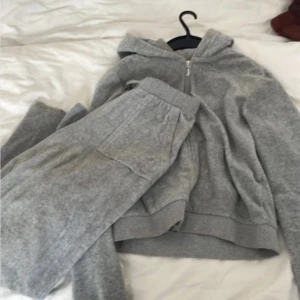 Grå hoodie och byxor i fleece - Mysig grå hoodie med dragkedja och matchande byxor i fleece. Perfekt för kalla dagar med sin mjuka och varma känsla. Hoodien har en praktisk huva och byxorna har bekväma fickor.