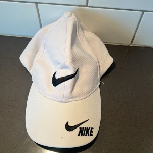 Vit keps  - Snygg vit keps med svart broderad logga framtill. Kepsen har en flexibel passform tack vare Flexfit-teknologin och är tillverkad i polyester. Perfekt för en sportig look.