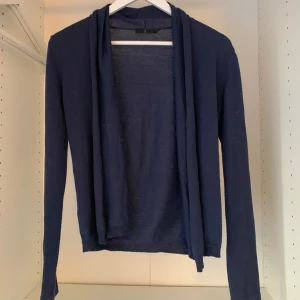 Mörkblå kofta från Åhléns - Säljer en stilren mörkblå kofta från Åhléns. Den har en öppen design utan knappar och är tillverkad i ett mjukt material. Perfekt för lager-på-lager under kyligare dagar.