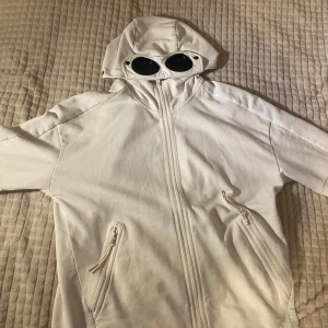 C.P company hoodie - Säljer en unik vit zip från C.P. Company med goggles i huvan.  dragkedja framtill och två fickor med dragkedjor. Perfekt för en stilren och modern look. väldigt bra skick