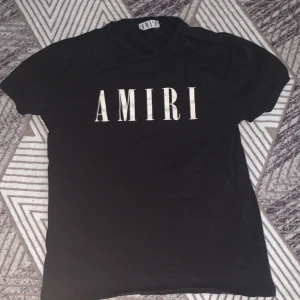 Svart t-shirt från Amiri - Snygg svart t-shirt från Amiri med stort vitt tryck på framsidan. Perfekt för en stilren och modern look. T-shirten har en klassisk passform och är kortärmad.