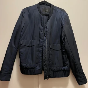 Mörkblå jacka från Opus - Snygg mörkblå jacka från Opus med dragkedja framtill och två stora fickor. Jackan har en stilren design med långa ärmar och elastisk nederkant för en bekväm passform. Perfekt för kyligare dagar.