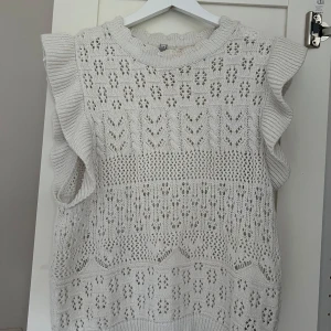 Cremevit stickad blus med volangdetaljer från Only - Säljer en söt vit stickad topp med vackra volangdetaljer vid ärmhålen. Toppen har ett fint hålmönster och är perfekt för lager-på-lager-stil. Passar bra till både jeans och kjol. Perfekt för vår och sommar! Inga defekter, köpt för 399 kr