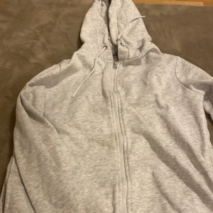 Grå hoodie från George - Säljer en bekväm grå hoodie från George med dragkedja och huva. Perfekt för en avslappnad stil. Den har långa ärmar och en klassisk passform. Perfekt för kyliga dagar!