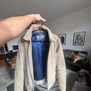 Säljer en stilren beige mockajacka från human scales. Jackan har en klassisk krage och dragkedja framtill. Insidan är fodrad med blått tyg vilket ger en snygg kontrast. Perfekt för en elegant look. Storlek M köpt på debut 