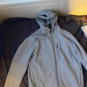 Grå hoodie från Sail Racing - Säljer en grå hoodie från Sail Racing med dragkedja och huva. Hoodien har jag haft i två veckor och använt den cirka 4 gånger under dom två veckorna men den är väldigt sann till storlek så jag rekommenderar den stort till alla som är M storlek