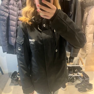 Svart jacka från Dope - Säljer en svart jacka från Dope med dragkedja och knappar. Jackan har en justerbar huva och flera praktiska fickor. Perfekt för kyligare väder och har en stilren design med logotypdetaljer på bröstet och ärmen.  en ny kostar mellan 1000 och 2000, den här har några fläckar från användning men inte jöttestora💗