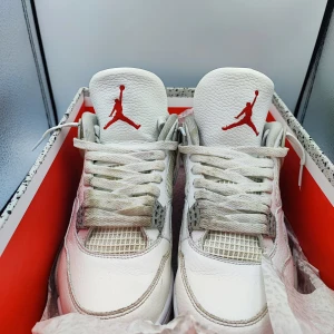 Nike Air Jordan 4 Retro - Säljer ett par Nike Air Jordan 4 Retro i vitt med grå och röda detaljer. Skorna har en klassisk design med snörning och synlig Air-dämpning i sulan. Perfekta för sneakerheads som älskar en stilren look. TVÄTTAR SNÖRARNA INNAN JAG SKICKAR 