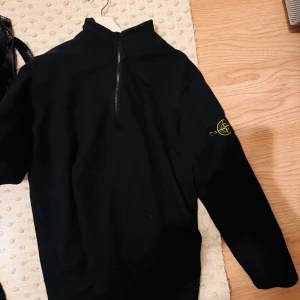 Svart tröja med dragkedja från Stone Island - Snygg svart tröja från Stone Island med halv dragkedja. Perfekt för en stilren och avslappnad look. Passar bra till både jeans och chinos. Storlek M