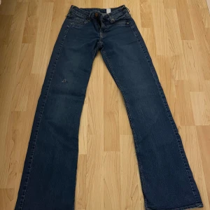 Blå bootcut jeans - Säljer ett par snygga blå bootcut jeans med låg midja. Perfekta för en avslappnad stil. De har klassiska femficksdetaljer och en bekväm passform. De har ett litet hål på knät men de är inte värsta.